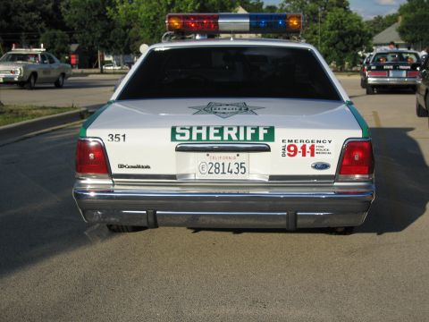 1991 Ford Crown Victoria - Rear view of a white police car with a light bar and SHERIFF markings.