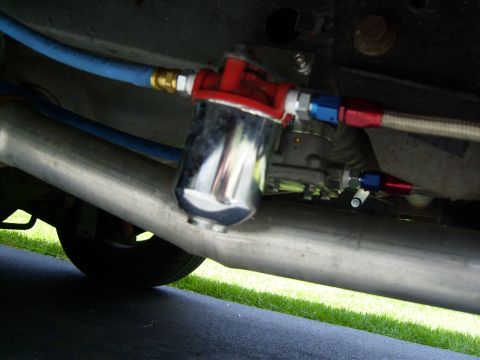 1972 Ford Ranchero - Underbody close-up of a frame-mounted inline fuel filter/regulator with a polished canister and red anodized housing, plumbed with braided…