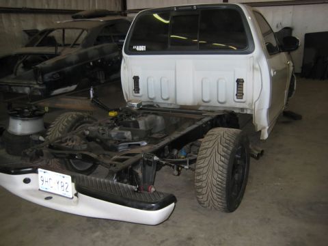 2007 Ford Mustang - A white pickup truck is shown with its chassis exposed, missing its bed and rear body panels. A license plate is visible on the detached re…