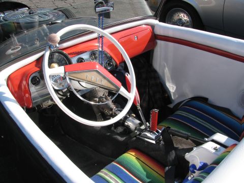1990 Ford Bronco - cockpit of an open hot rod shows a white steering wheel, red Ford dashboard and a colorful serape-striped bench seat.