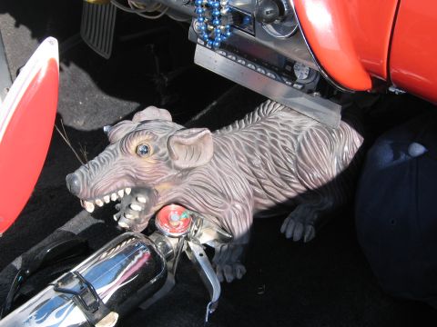 1990 Ford Bronco - detailed carved figurine of a snarling rat is mounted on a chrome bar beside red bodywork inside a vehicle.