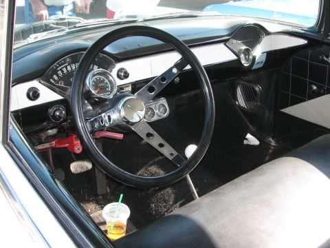 1990 Ford Bronco - black-and-white classic car interior shows a drilled steering wheel, round gauges and a Chevrolet-scripted dash, with a drink in the cup.