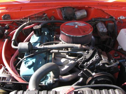 1990 Ford Bronco - engine bay shows a teal engine block topped by a red-and-chrome air cleaner, framed by orange inner fenders.