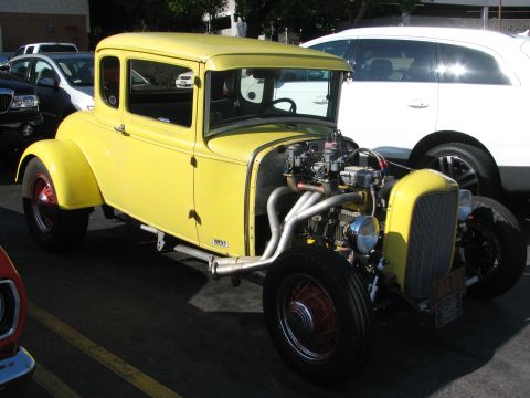 1990 Ford Bronco - yellow five-window coupe hot rod with an exposed twin-carb V8, zoomie headers and wire wheels sits at a show.