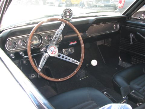 1990 Ford Bronco - classic muscle car interior shows a wood-rimmed three-spoke steering wheel, round gauges and black trim.