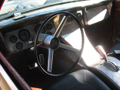 1990 Ford Bronco - interior of a classic truck showing a chrome four-spoke steering wheel, round dashboard gauges, and black bucket seat in raw sunlight.