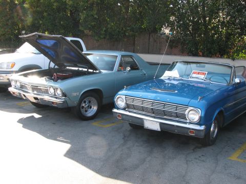 1990 Ford Bronco - blue Chevrolet El Camino with its hood up sits beside a blue Ford convertible with a For Sale sign at a car show.
