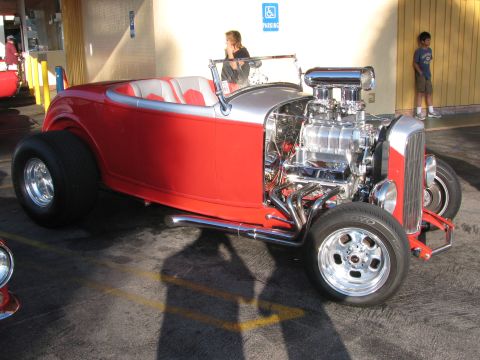 1990 Ford Bronco - red highboy hot rod roadster with a chromed blown V8 engine and white interior sits in a covered lot.