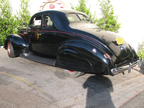 1990 Ford Bronco - black late-1930s coupe shown from the rear with fender skirts and a red pinstripe, parked outdoors.