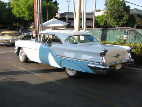 1990 Ford Bronco - two-tone light blue and white 1950s Oldsmobile two-door hardtop with chrome fins and trim, parked in a lot at dusk.