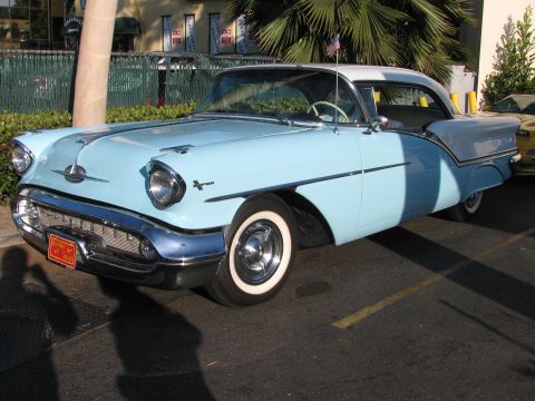 1990 Ford Bronco - two-tone light blue 1950s Oldsmobile hardtop with chrome grille, whitewall tires and a white roof, parked outdoors.