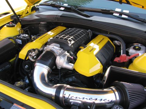 1990 Ford Bronco - supercharged V8 engine bay with a Hennessey-branded chrome intake tube, yellow covers and a polished supercharger.