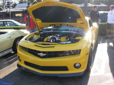 1990 Ford Bronco - yellow Chevrolet Camaro SS with its hood raised showing a supercharged engine, parked at a car show with onlookers.