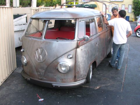 1990 Ford Bronco - lowered bare-metal Volkswagen split-window bus with red interior, parked on asphalt as two men stand at the door.