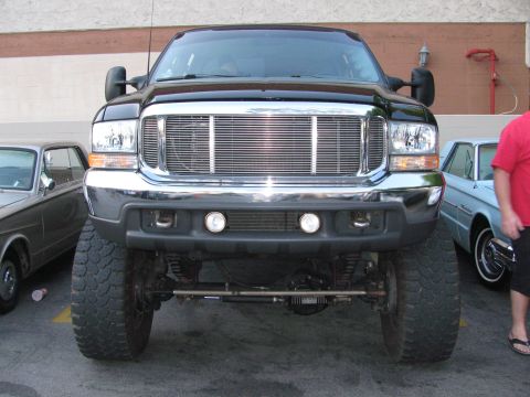 1990 Ford Bronco - lifted black Ford Super Duty pickup viewed head-on, showing its chrome grille, solid front axle and large off-road tires.