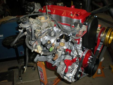 Suzuki Samurai - A rebuilt four-cylinder engine on an orange engine stand, painted red with a red valve cover and freshly cleaned aluminum intake and access…