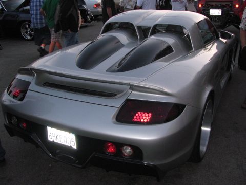 1990 Ford Bronco - rear of a silver Porsche Carrera GT showing its twin engine cover humps, rear wing and tail lights at a meet.