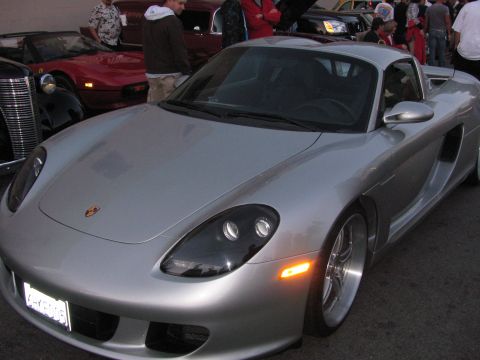 1990 Ford Bronco - silver Porsche Carrera GT viewed from the front, parked beside a red Ferrari at a car show with people behind.