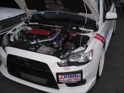 1990 Ford Bronco - white Mitsubishi Lancer Evolution with its hood raised showing a tuned engine, parked at a show with a dealer plate.