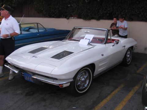 1990 Ford Bronco - white 1960s Chevrolet Corvette Sting Ray convertible with red interior, parked at an outdoor car show beside a judge.