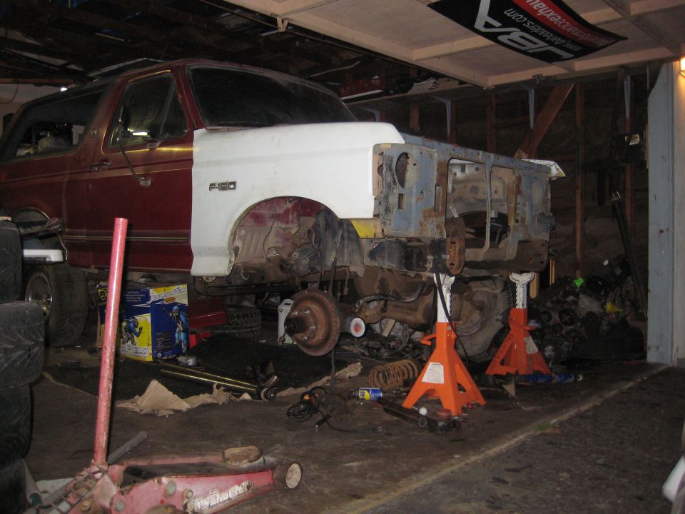 1990 Ford Bronco with front end disassembled, on jack stands in a garage
