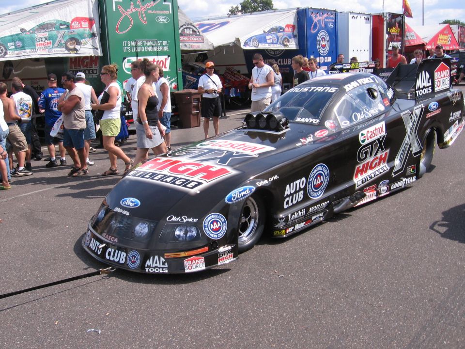 Black drag racing car with 'Castrol GTX High Mileage' livery, parked on asphalt with spectators in background