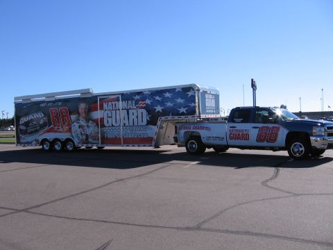 1998 GMC Sierra 1500 - Truck and trailer display National Guard and racing team sponsorship graphics under a clear sky.