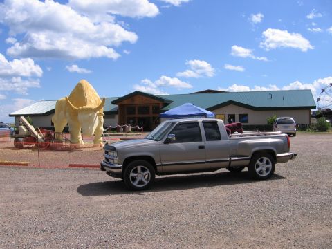1998 GMC Sierra 1500 - A 1998 GMC Sierra 1500 is parked outside a building with a large bison statue and a Ferris wheel in the background.