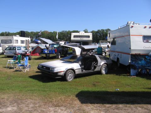 1998 GMC Sierra 1500 - A silver DeLorean DMC-12 is parked in a grassy field with several RVs and tents visible.