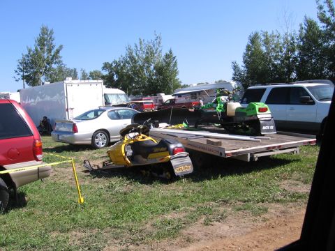 1998 GMC Sierra 1500 - A scene with two snowmobiles loaded onto a trailer, surrounded by other vehicles and trailers under a clear blue sky.