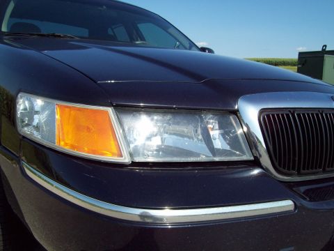 1999 Mercury Grand Marquis - Close-up of the front driver-side corner of a very dark blue Mercury Grand Marquis, showing its chrome-framed waterfall grille, clear compo…
