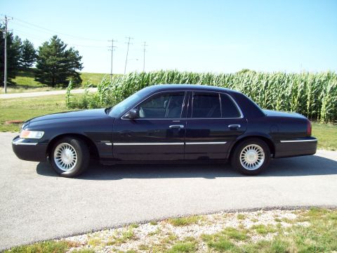 1999 Mercury Grand Marquis - A dark blue 1999 Mercury Grand Marquis sedan is parked on a paved surface with a cornfield in the background.