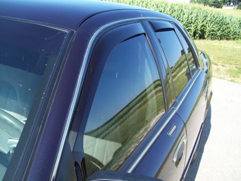 1999 Mercury Grand Marquis - Side view of a dark sedan with window ventshades installed, set against a rural backdrop.