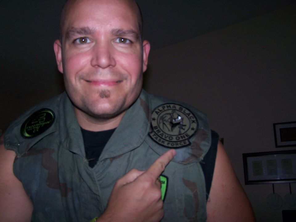 Man pointing to a patch on his vest that says "ALPHA BLACK BRAVO ONE TASK FORCE"
