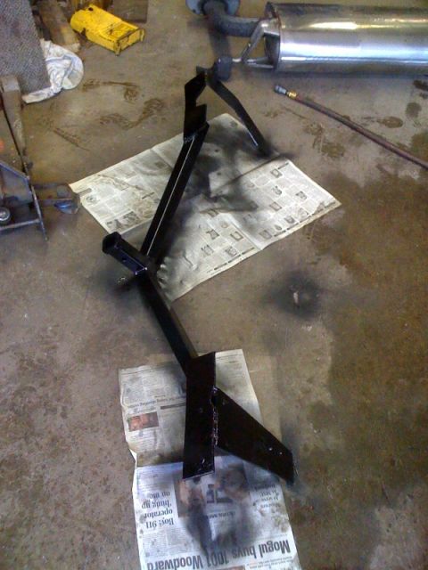 2010 Hyundai Genesis - A black metal frame, likely an exhaust part, is laid out on newspaper in a workshop setting.
