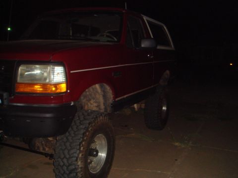 1992 Ford Bronco - This red SUV is parked outside at night, showing off its large tires and lifted suspension.