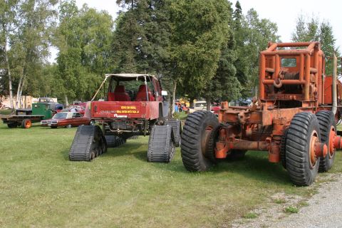1987 Suzuki Samurai - A modified red vehicle with tracks sits next to a large orange industrial vehicle on a grassy field.