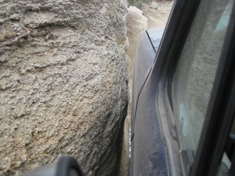 1986 Ford Bronco - A dark SUV navigates a tight passage between two large rocks on a trail.