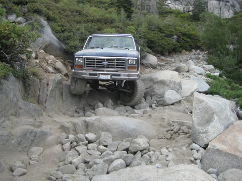 1986 Ford Bronco - 1986 Ford Bronco tackles a challenging off-road path with large rocks.