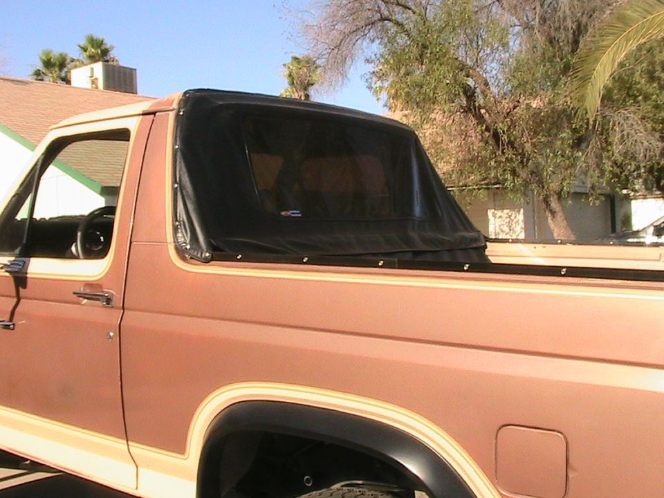 Side view of a tan Ford Bronco with a black soft top covering the rear