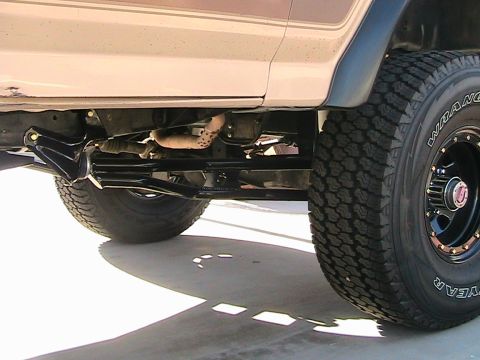 1985 Ford Bronco - The underside of a vehicle shows its suspension components and off-road tires.