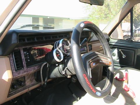 1985 Ford Bronco - The interior of a vehicle is shown, aftermarket gauges and a steering wheel cover with 'Racing' text.