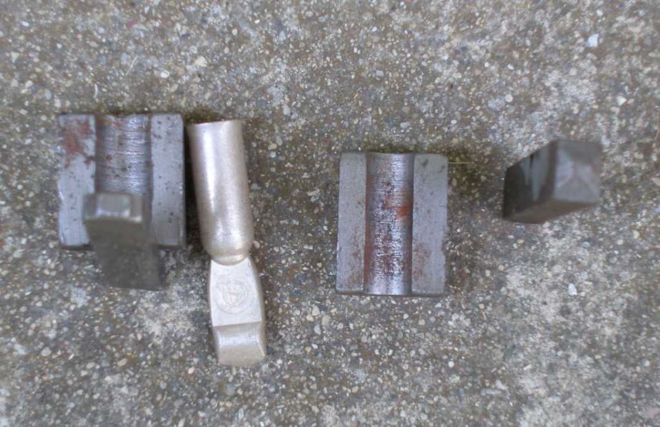 four metal electrical connectors on concrete, one has a circular logo