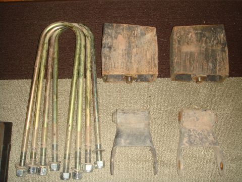 1992 Ford Bronco - Used lift hardware laid out on carpet: four long yellow zinc-plated U-bolts with nuts on the left, a pair of tall cast leaf-spring lift blo…