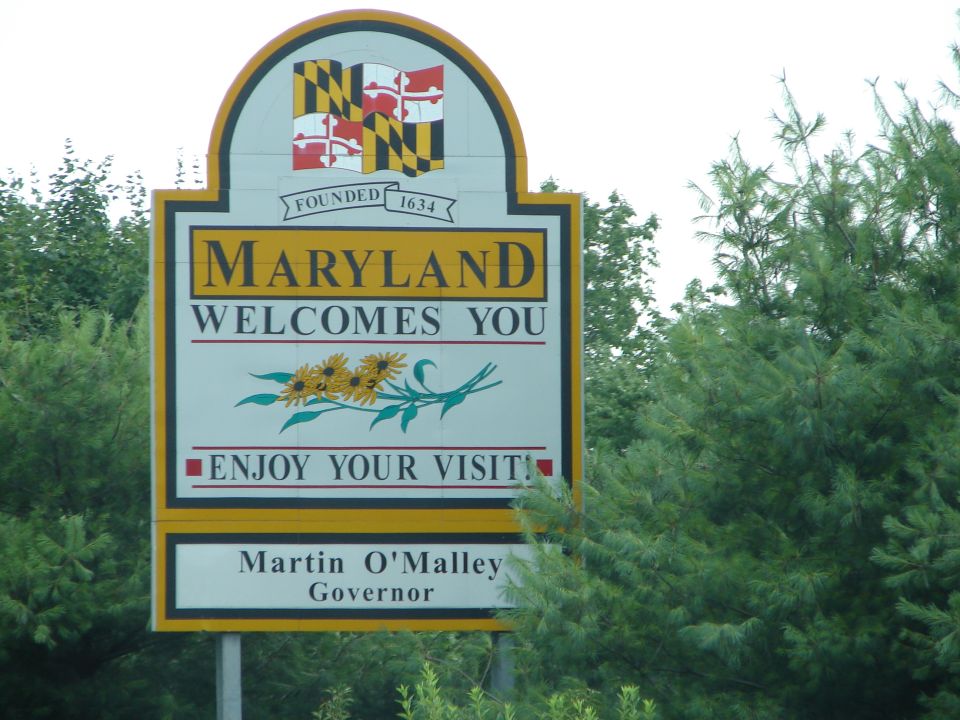 Maryland welcome sign with state flag and sunflowers. Says 'Maryland Welcomes You' and 'Enjoy Your Visit'