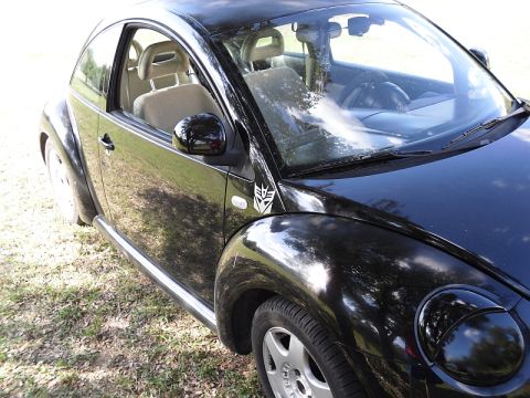 1999 Volkswagen Beetle - A black Volkswagen Beetle is parked on a grassy area, showing a Transformers logo on its front fender.