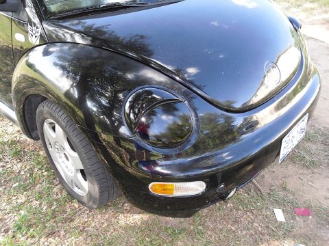 1999 Volkswagen Beetle - A black Volkswagen Beetle is viewed from the front quarter, revealing its distinctive rounded headlights and fender emblem.