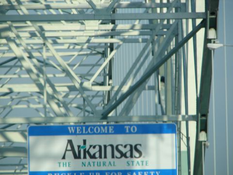 1992 Ford Taurus - A sign welcomes visitors to Arkansas, situated beneath a large metal bridge.