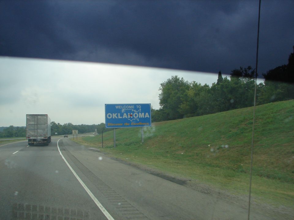 Driving past a welcome sign for Oklahoma on the highway, with a semi-truck on the left