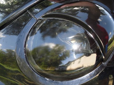 1999 Volkswagen Beetle - Close-up of a black headlight, reflecting the surrounding environment.
